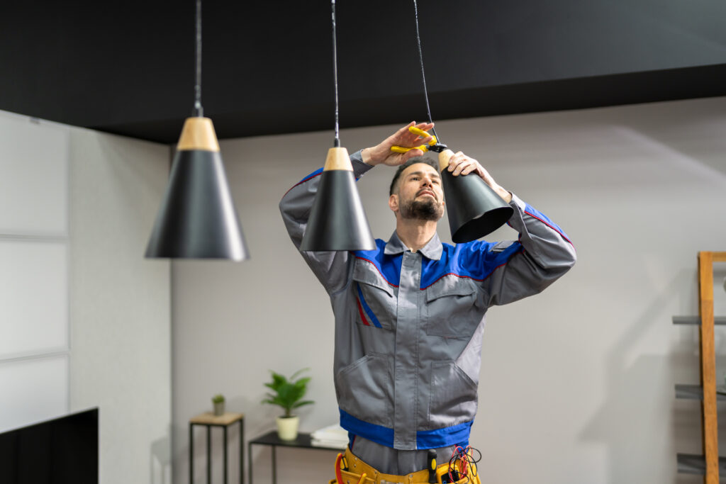 Electrician installing a new black pendant light in a home.